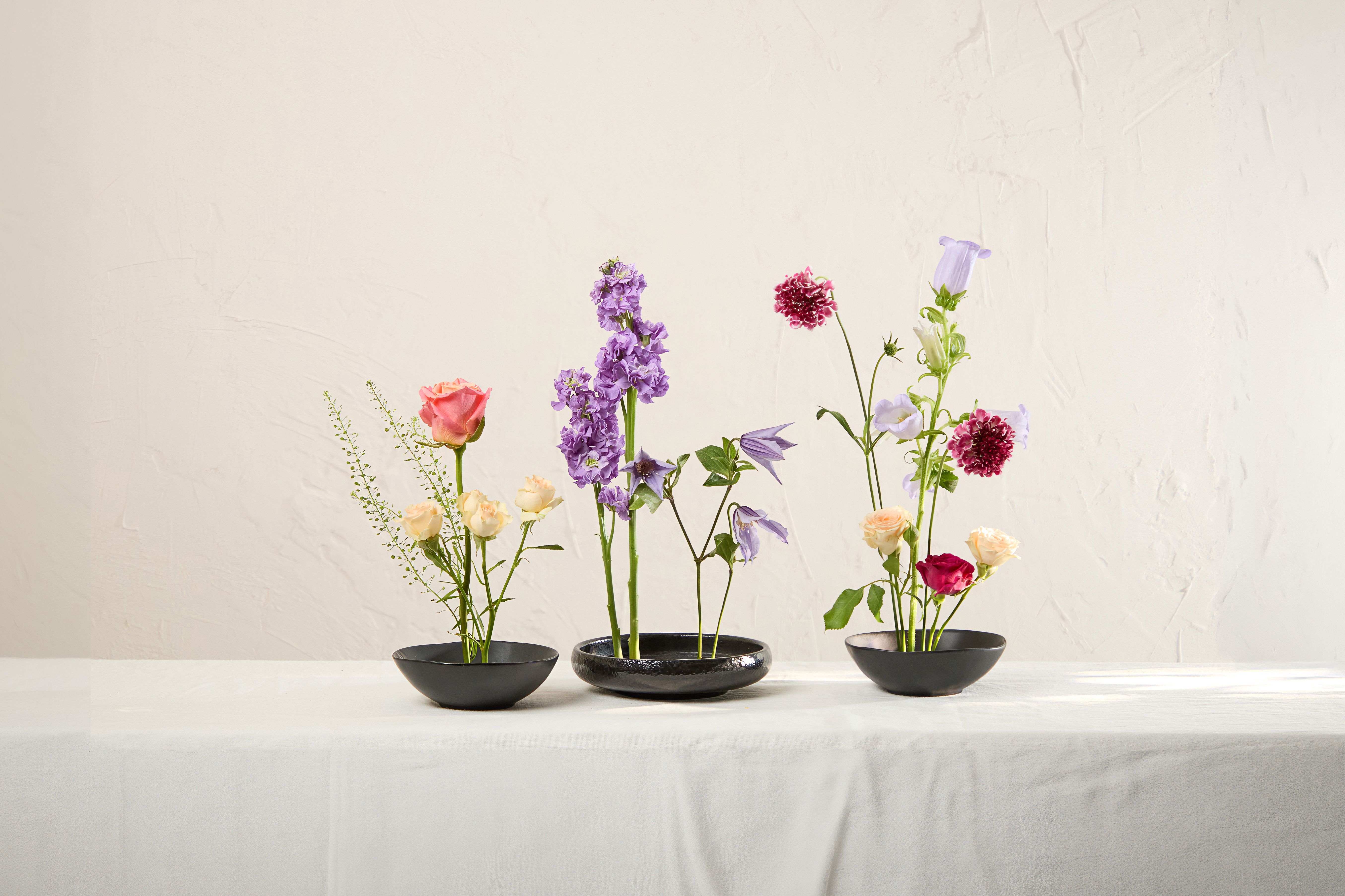 Peach, orange, red and purple flowers arranged in three black flower frogs