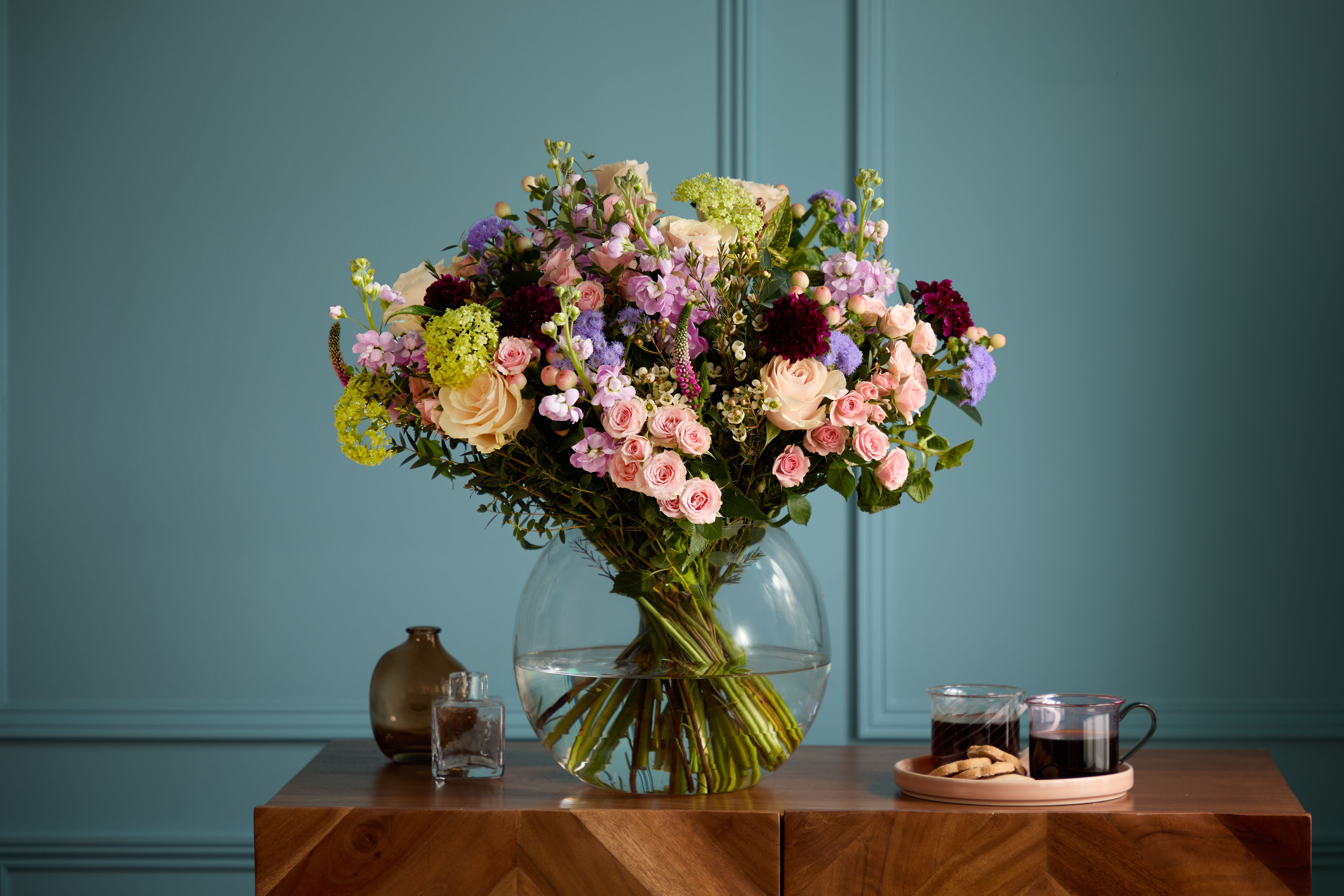 Arena Flowers' 'Secret Garden' bouquet, a luxury arrangement of pink, purple and green, in a vase against blue wall