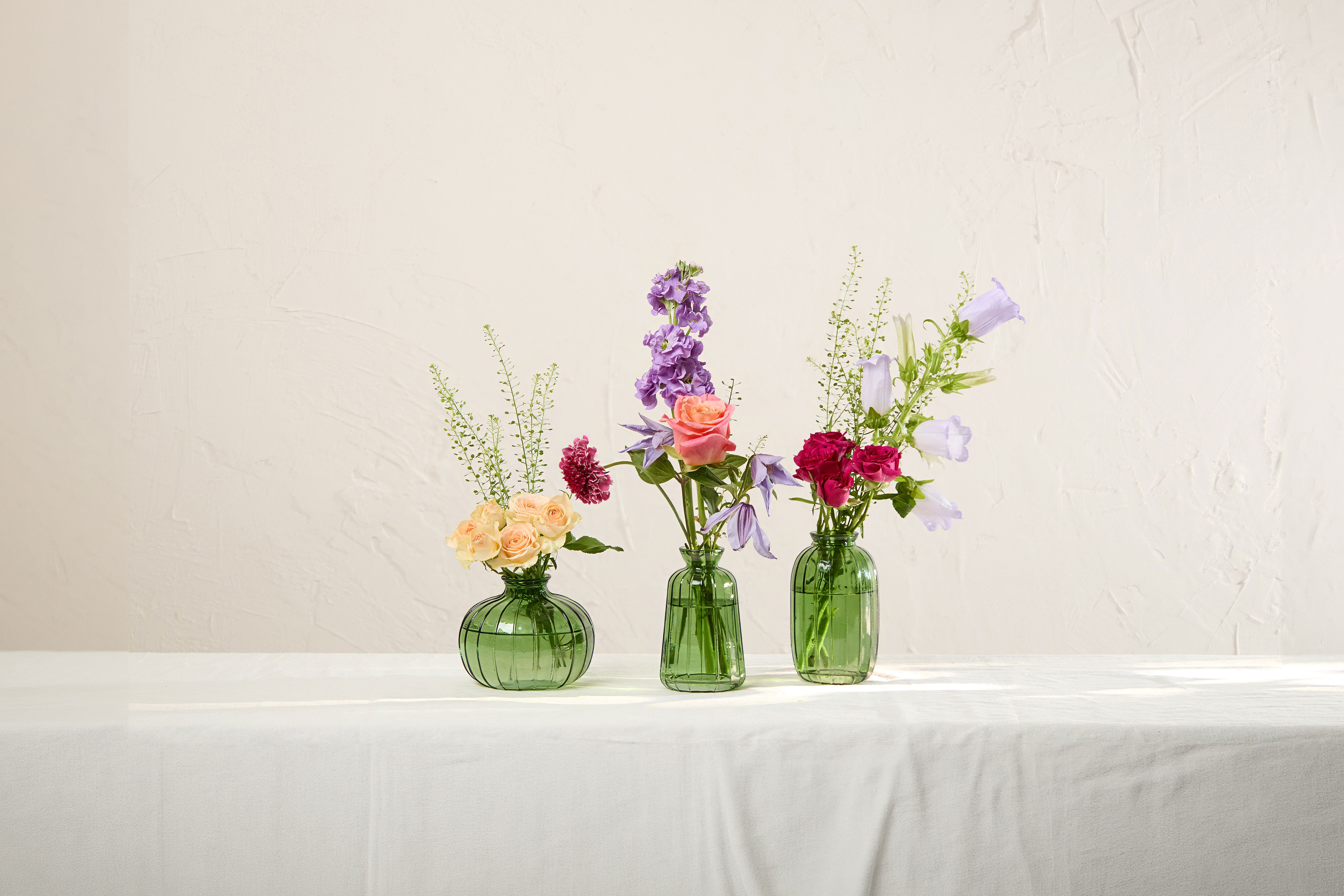 Peach , orange, red and purple flowers arranged in three green glass bud vases
