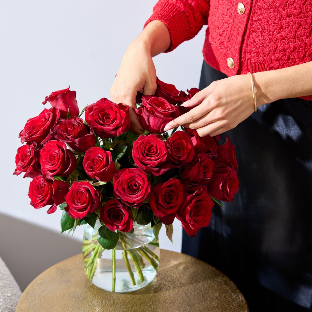 A bouquet of Fairtrade red roses on a table. A woman wearing a red cardigan is arranging them.